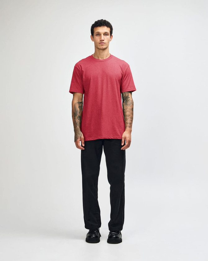 A unisex CVC short sleeve t-shirt in red, paired with black cargo pants. The model displays a casual pose.