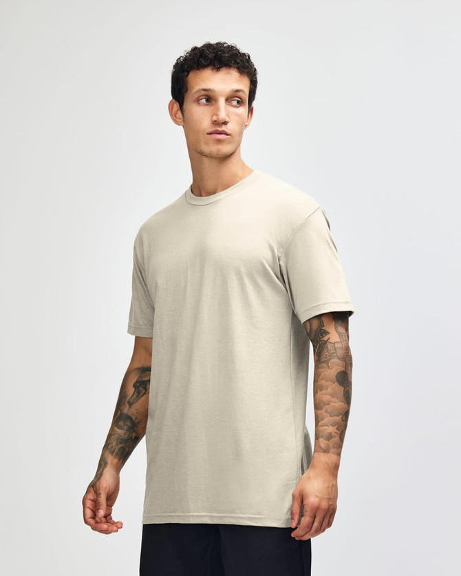 A unisex beige CVC short sleeve T-shirt displayed on a model, featuring a logo.