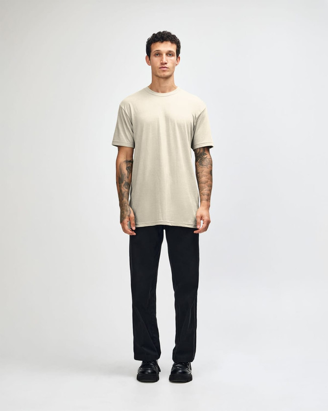 A unisex short sleeve T-shirt in beige, paired with black cargo pants, featuring a logo on the shirt.
