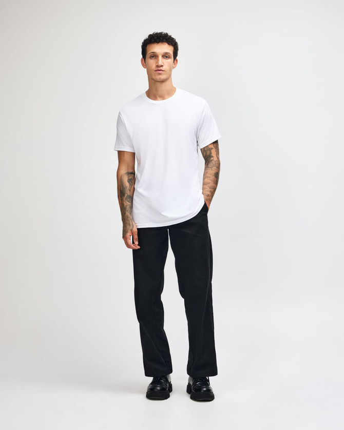 A young man wearing a plain white unisex short sleeve t-shirt and loose blue jeans, standing against a white background.