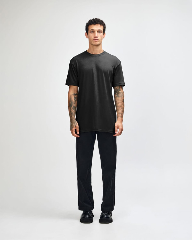 A black unisex short sleeve t-shirt worn with light blue baggy jeans and black sneakers. The model poses against a plain background.