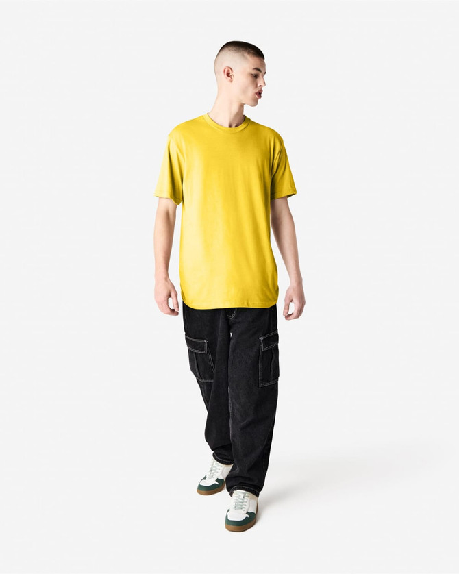 A model wearing a yellow unisex short sleeve T-shirt with black cargo pants and green and white shoes, featuring a logo.