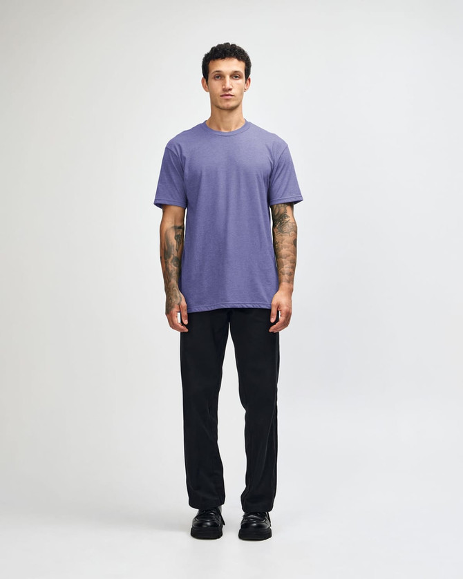 A unisex short sleeve t-shirt in purple, worn by a model with black pants and sneakers, featuring a logo.