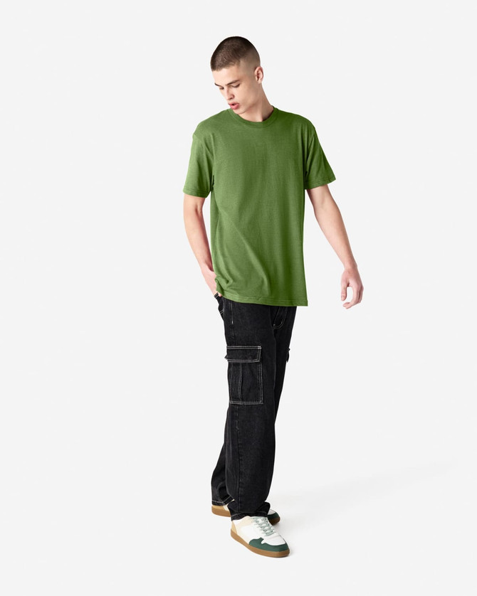 A model wearing a green unisex CVC short sleeve T-shirt paired with black cargo pants and sneakers.