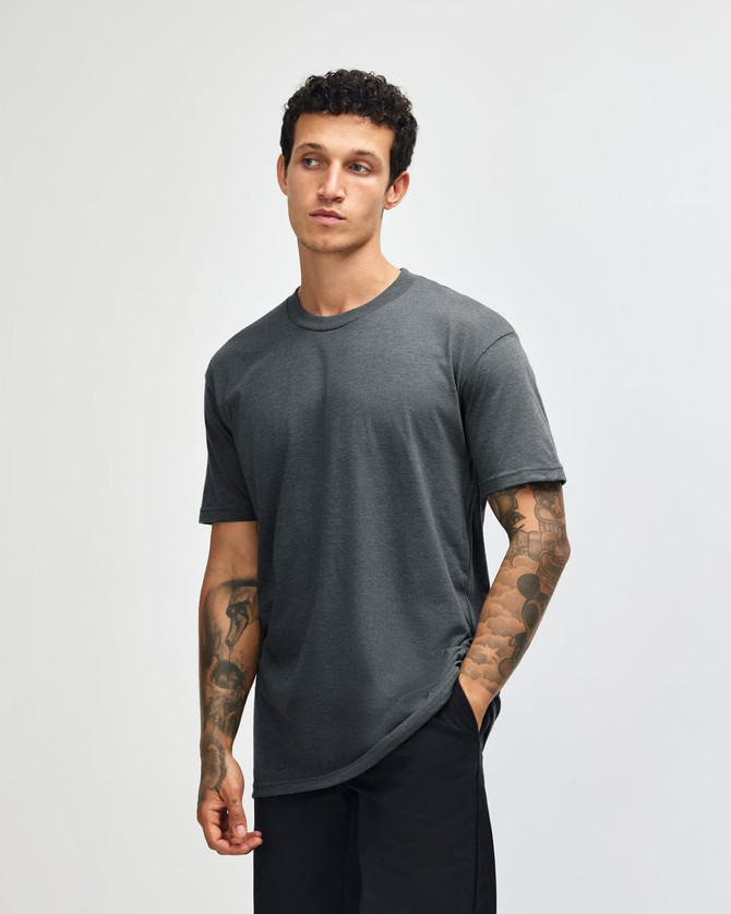 A unisex short sleeve t-shirt in grey, featuring a logo, displayed on a model with tattoos.