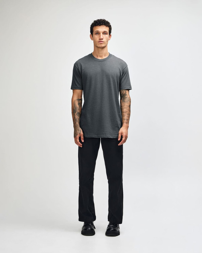 A grey unisex CVC short sleeve t-shirt displayed on a model, paired with black trousers, and featuring a logo.