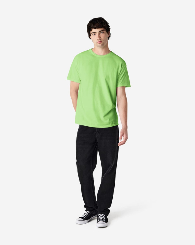 A man stands wearing a bright green Gildan Heavy Cotton adult T-shirt and black jeans, with a logo on the shirt.