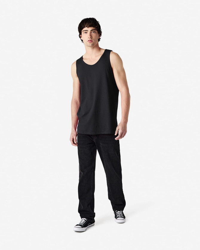 A black Gildan Heavy Cotton adult tank top worn by a model, paired with black trousers and sneakers.