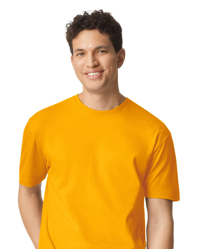 A smiling young man wearing a vibrant yellow Gildan Softstyle adult t-shirt with a logo on it.
