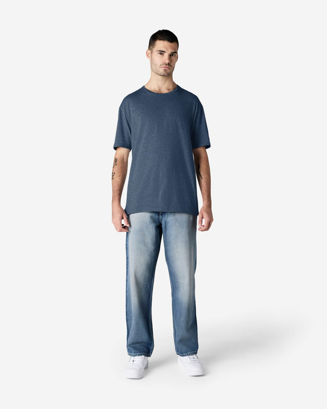 A model wearing a navy Gildan Softstyle adult T-shirt paired with light blue jeans and white shoes.