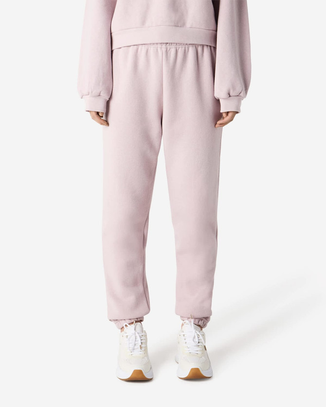 Unisex sweatpants in soft pink, featuring an elastic waistband and cuffs, shown with a pair of sneakers.