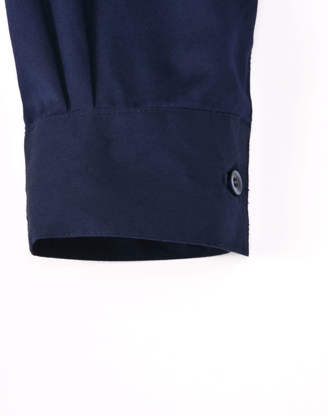 A navy long-sleeve work shirt featuring a closed front and buttoned cuff detail. It has a logo.