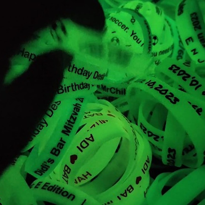 A collection of neon green silicone wristbands with various printed messages, glowing in the dark.