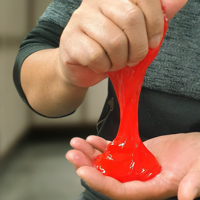 A person holding and squeezing bright red slime, with some slime dripping onto the palm.