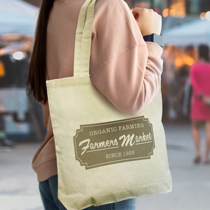 A yellow cotton tote bag with a logo, worn over the shoulder by a person in a casual outfit.