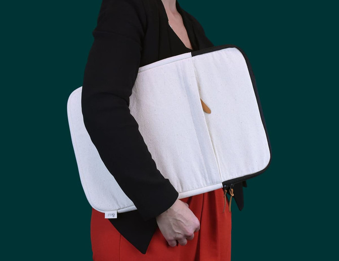 A laptop sleeve in cream with a black zipper, held by a person wearing a black top and red skirt.