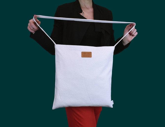A white tote bag with a long handle, featuring a logo on the front, held by a person wearing a black top.