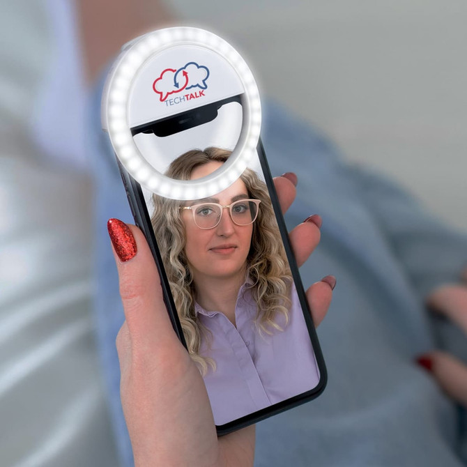 A phone with a circular ring light attached, featuring a logo, displaying a person's face.