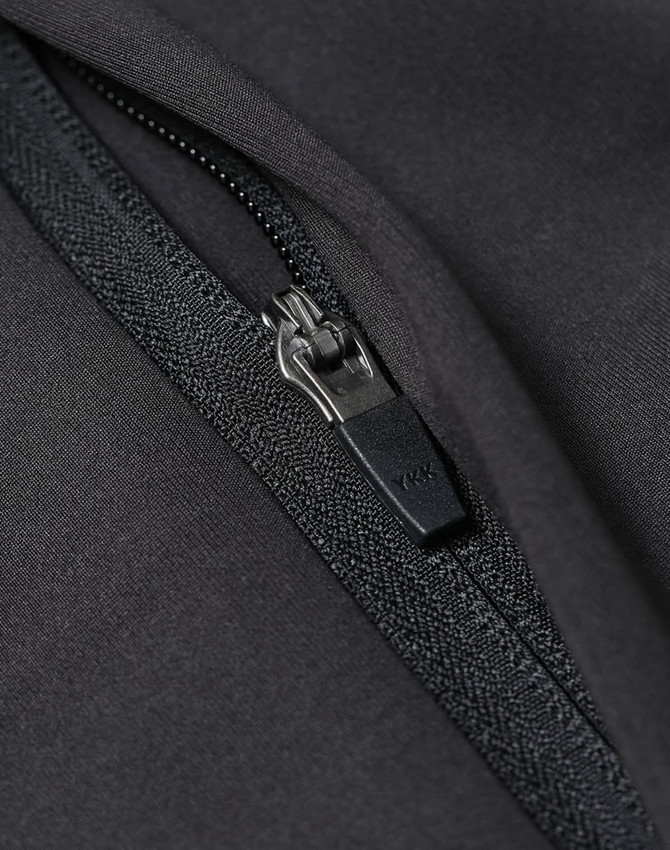 A close-up of a black softshell jacket featuring a zip with a branded pull tab.