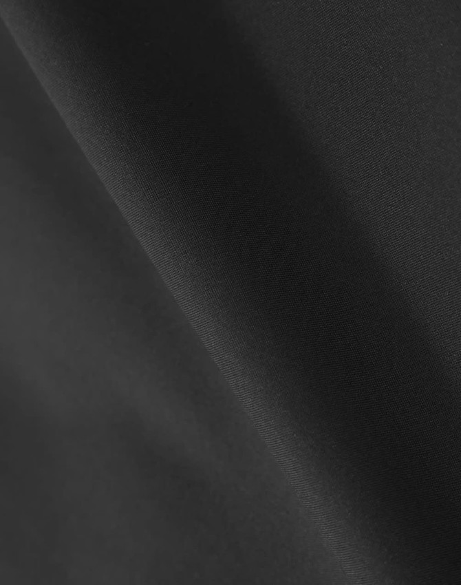 A close-up of black quilted fabric, highlighting its texture and waterproof qualities. The fabric has a smooth appearance.