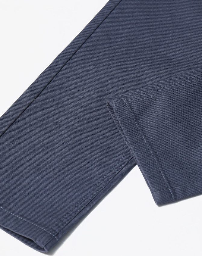 A close-up of navy blue flexi chino pants showing the stitching and hem details, including a logo.