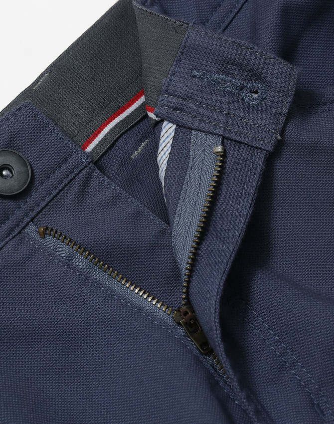 A close-up of navy blue ladies' chino pants featuring a zip fly and button closure, with a logo on the waistband.