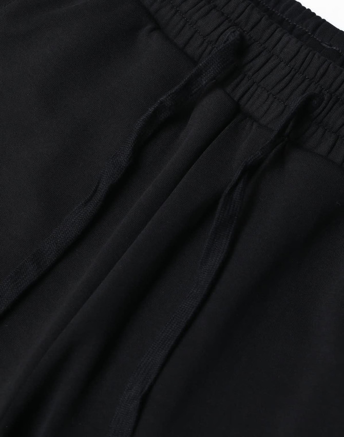 A close-up view of black unisex sweatpants featuring an elastic waistband and drawstrings. The image includes a logo.