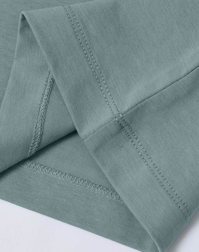A close-up of a light green premium cotton T-shirt, highlighting the sleeve and stitching details. The shirt has a logo.