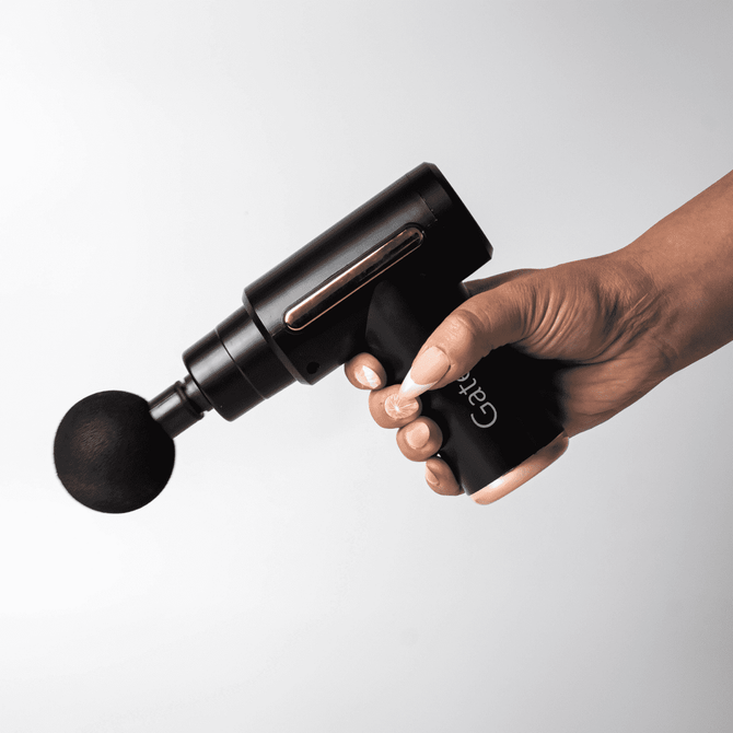A black massage gun with a spherical attachment held in a hand, featuring a sleek design and a logo.