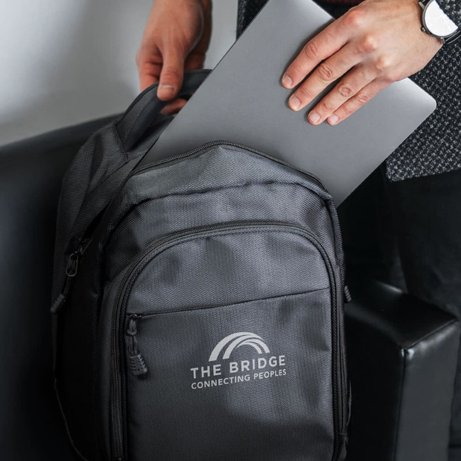 A grey laptop backpack being held while a silver laptop is being placed inside. The backpack has a logo.