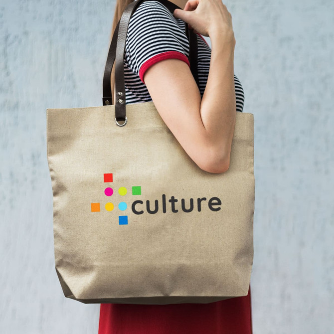 A beige tote bag with a logo and colourful dots, held by a person wearing a striped top.