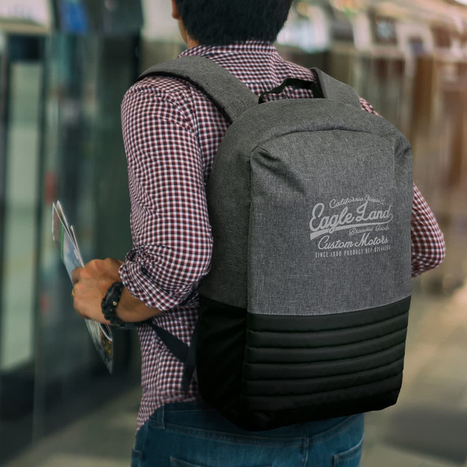 A grey and black backpack with padded straps and a logo, carried by a person in a checked shirt.
