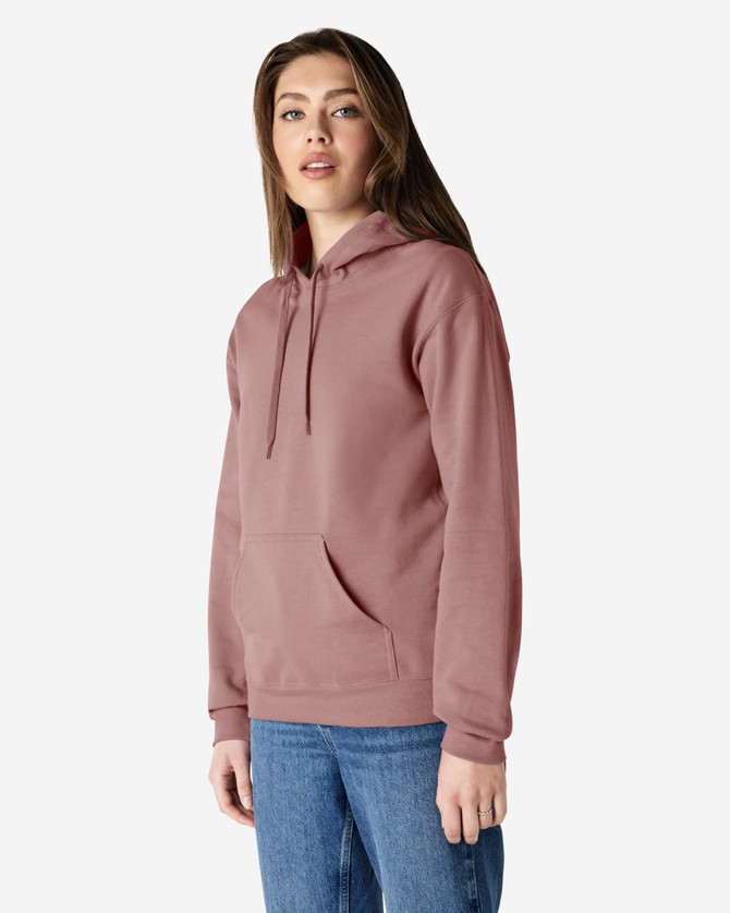 A person stands wearing a pink hooded sweatshirt with a front pocket and a drawstring hood.