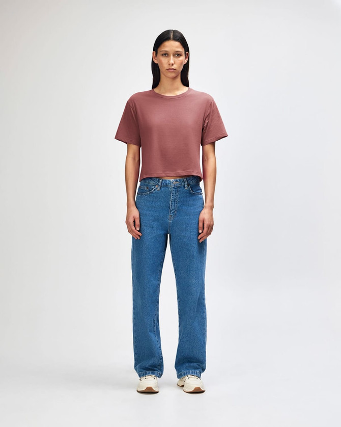 A woman's boxy t-shirt in rose, paired with light blue cargo jeans, featuring a logo on the shirt.
