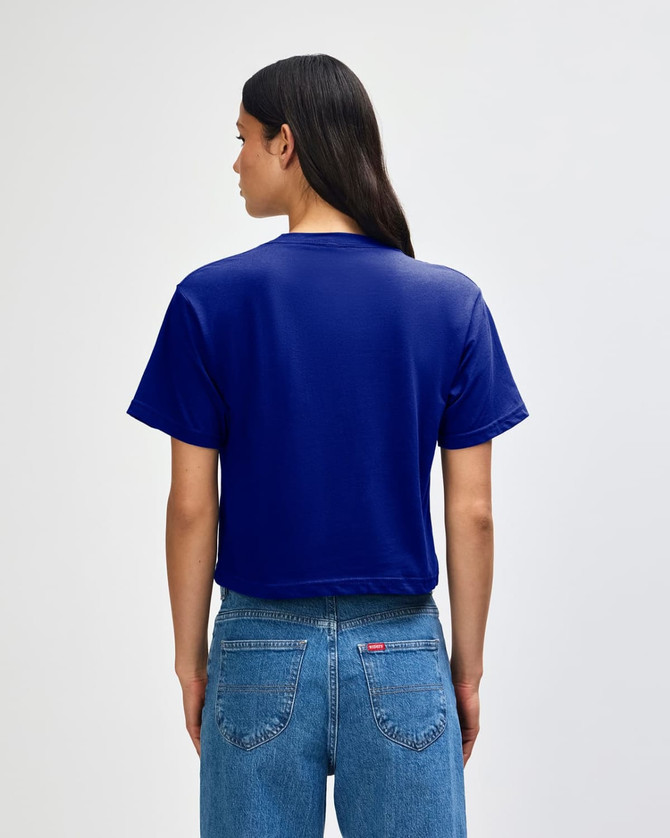 A blue boxy t-shirt with short sleeves and a back view. The model wears high-waisted jeans and has curly hair.