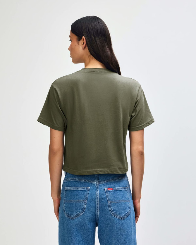 A back view of a women's olive green boxy T-shirt, paired with light blue cargo jeans. Features a logo.