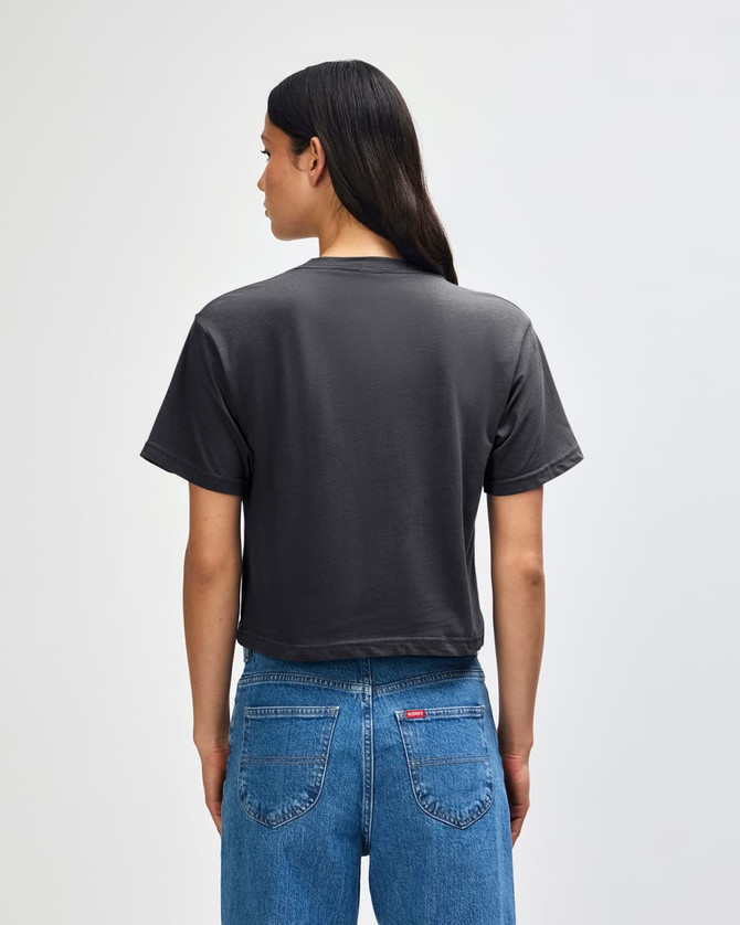 A grey boxy t-shirt is worn by a person with curly hair, standing with their back to the camera.