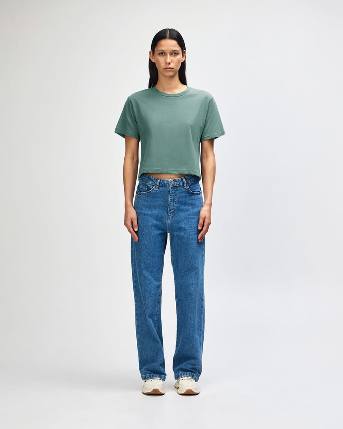 A model wears a green boxy t-shirt with light blue cargo jeans and sneakers, featuring a casual style.