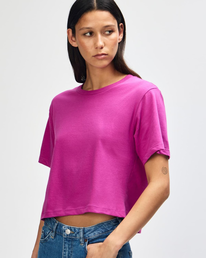 A woman wearing a bright pink boxy t-shirt, featuring a crew neck and short sleeves. The shirt has a logo.