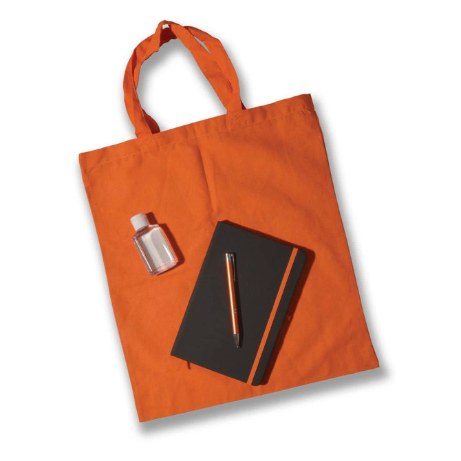 An orange tote bag holds a small clear bottle, a black notebook, and an orange pen.