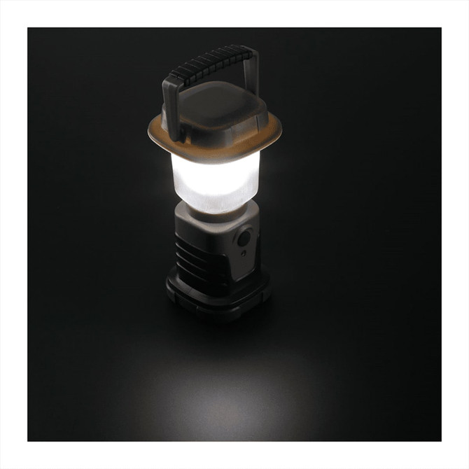 A mini camping lantern in grey and black with a transparent light dome and a handle on top.