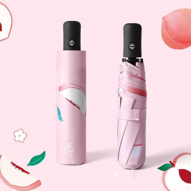 A pink umbrella with a peach design, displayed both open and in its case, featuring a black handle and branding.