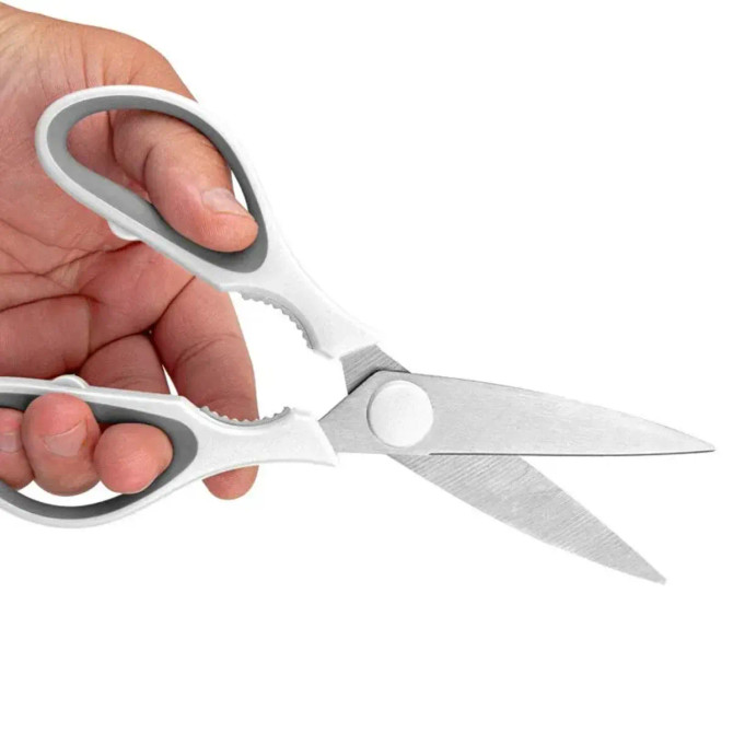 Kitchen scissors with stainless steel blades and a grey and white grip, held in a hand. Features a magnetic holder.