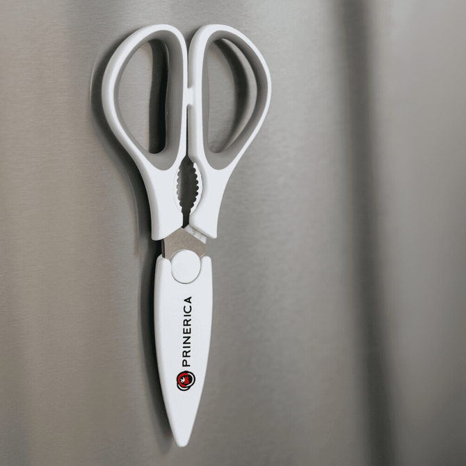 Kitchen scissors with a white handle and magnetic holder, mounted on a metallic surface. Features a logo.