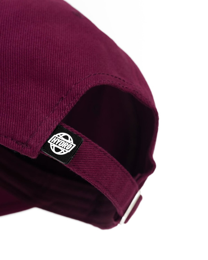 A maroon cap with a branded label on the side, featuring a curved peak and adjustable strap.