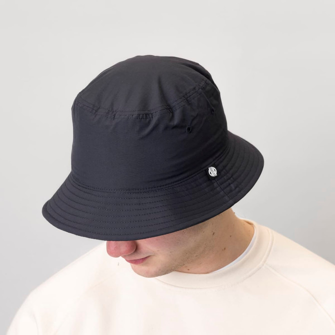 A black chino cotton twill bucket hat featuring a small logo, worn by a person with a neutral background.
