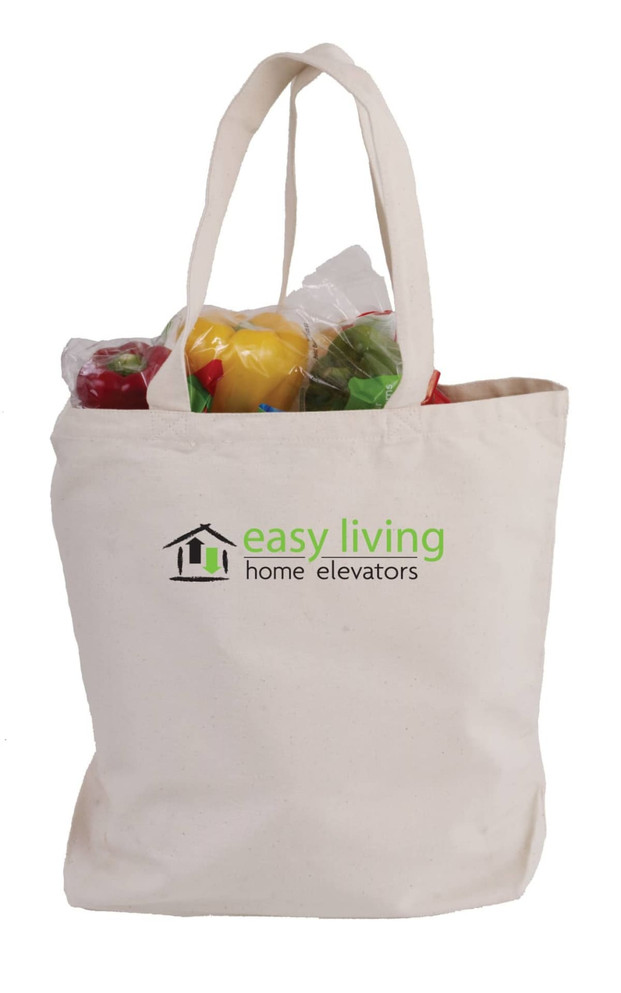 A cream canvas tote bag with two handles, containing various colourful vegetables and featuring a logo.