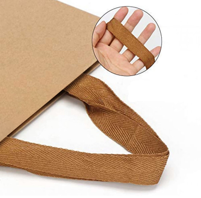 A brown recycled paper bag with a textured paper webbed handle, displayed with a hand holding the handle.