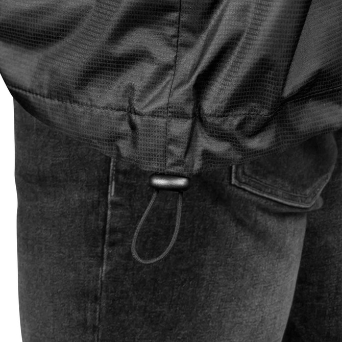A close-up of a black windbreaker jacket's hem with an adjustable drawcord, paired with denim jeans.