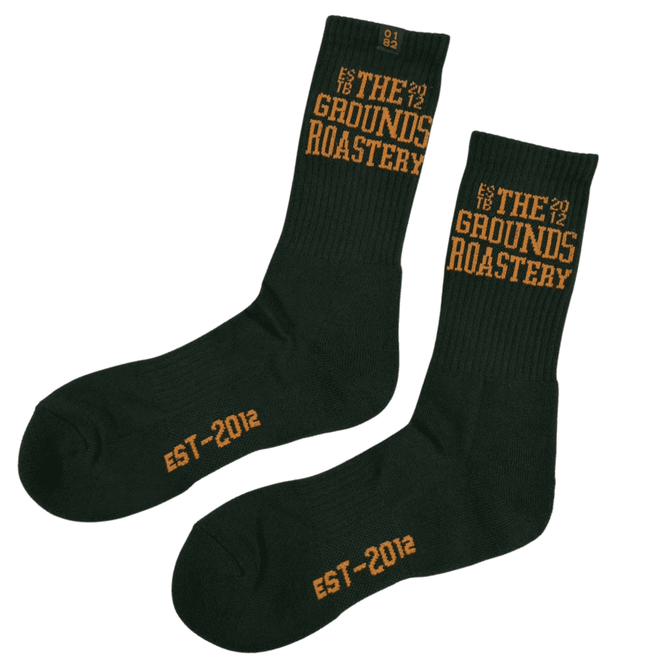 A pair of dark green socks with orange text, featuring branding and establishment year details.